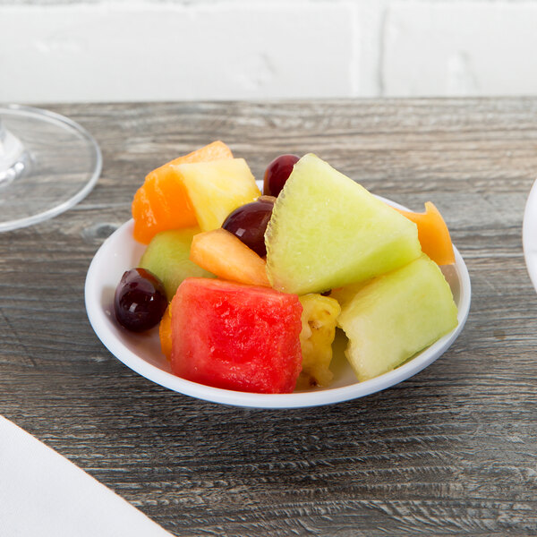 A Thunder Group white melamine plate with a bowl of fruit on a wood table.