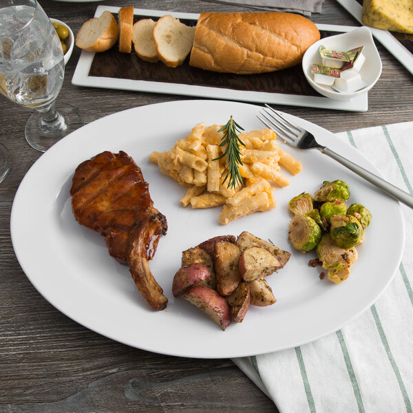 A white oval melamine platter with meat, potatoes, and bread on a table.