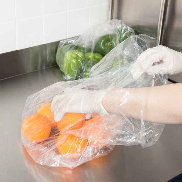 A person in gloves putting oranges in a plastic bag.