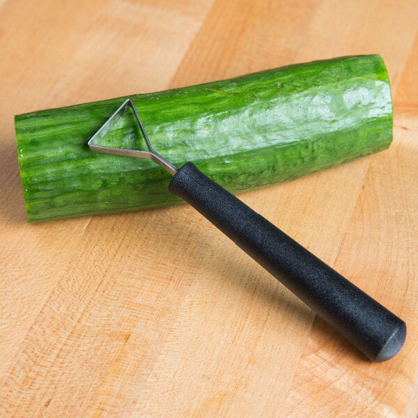 A cucumber garnished with a triangle decorator knife on a cutting board.