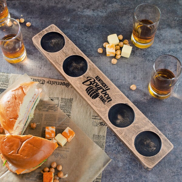 A wooden board with a Reserve by Libbey Kentucky Bourbon Trail Tasting Flight and a sandwich.