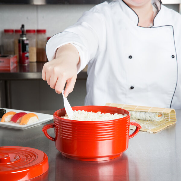 A person in a chef's uniform serving rice from a red Thunder Group rice container with a spoon.