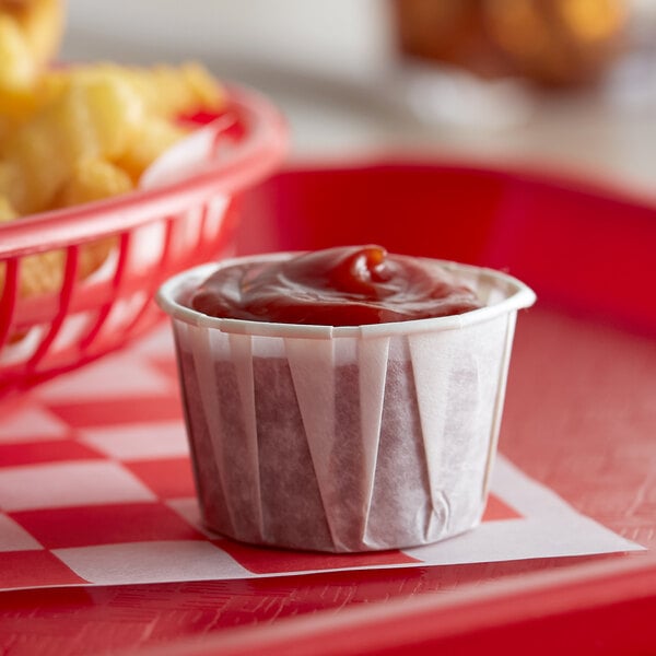 A small container of ketchup and french fries on a red tray.