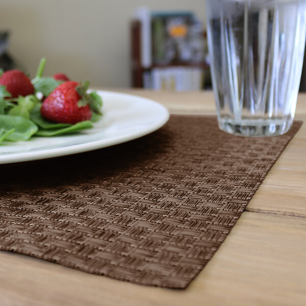 A plate of food and a glass of water on a brown woven vinyl rectangle placemat.