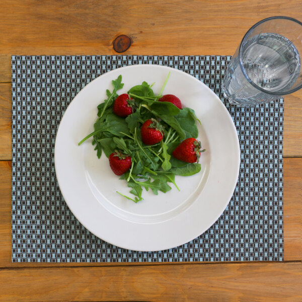 An Aqua and brown woven vinyl placemat on a table with a plate of salad and a glass of water.