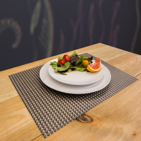 A rectangle pewter and copper woven vinyl placemat with a plate of fruit on a table.