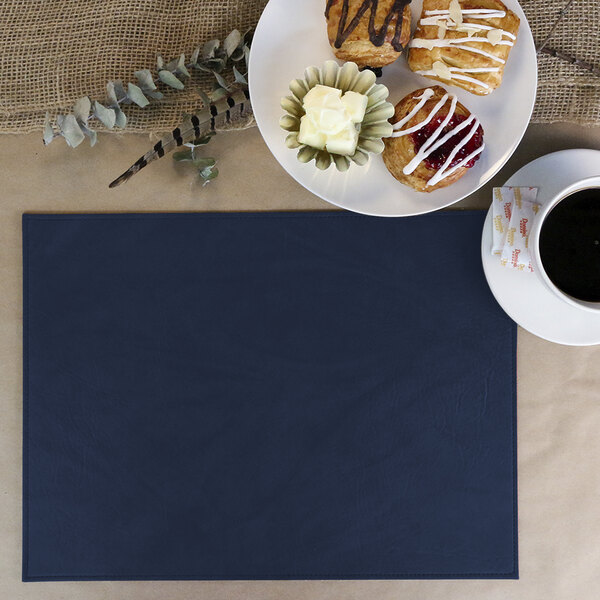 A navy H. Risch Harley faux leather placemat with a plate of pastries and a cup of coffee.