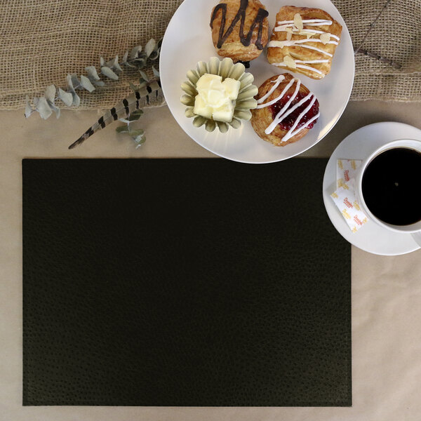 A black H. Risch Inc. faux leather placemat on a table with coffee and donuts.