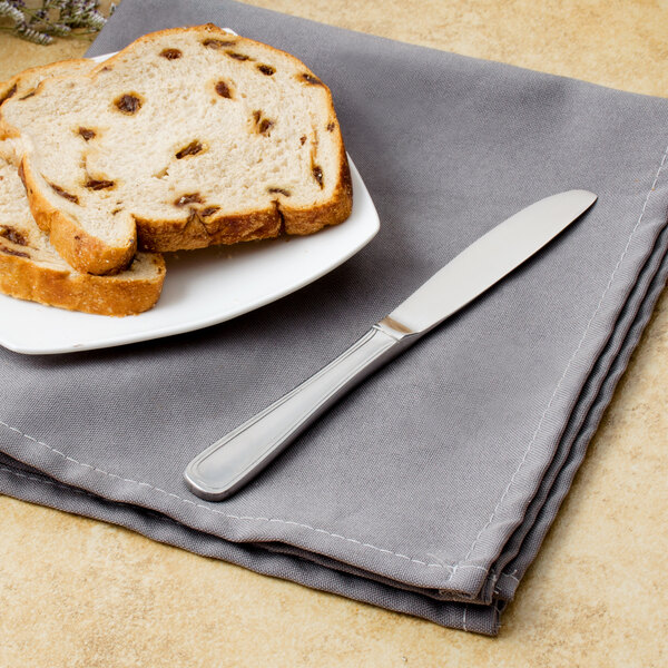A Walco stainless steel butter knife on a plate with a piece of bread.