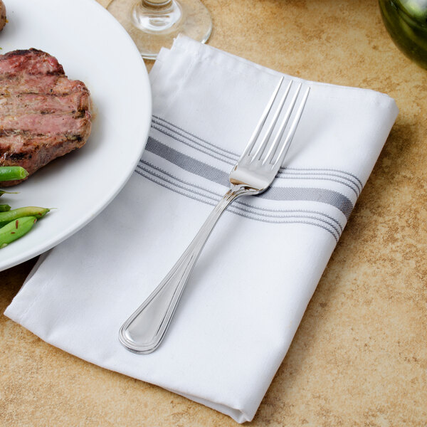 A Walco stainless steel dinner fork on a napkin next to a plate of food.