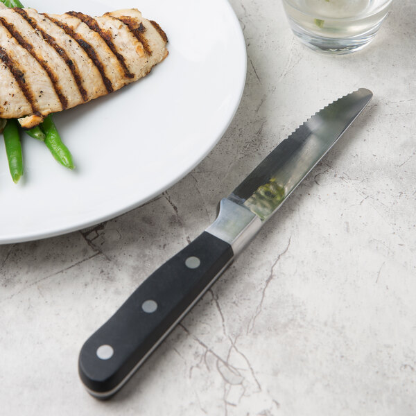 A Libbey stainless steel steak knife on a plate of food with a glass of water.
