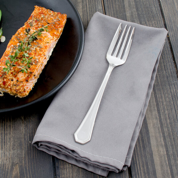 A plate of food with a piece of salmon and a Walco Prim stainless steel fish fork on a table.