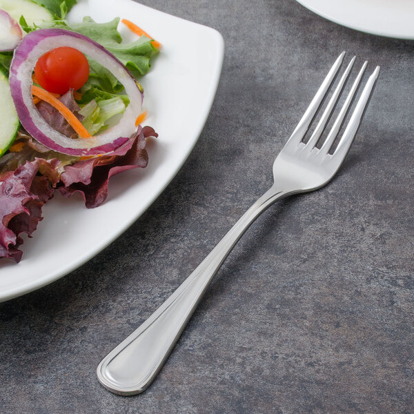 A Walco stainless steel salad fork on a plate of salad.