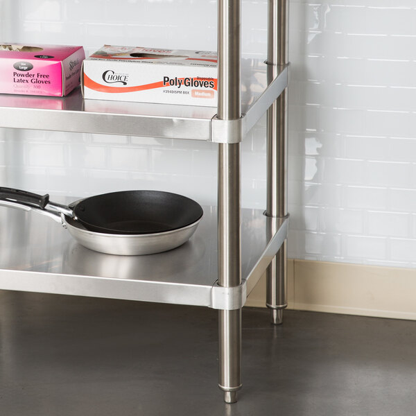 A stainless steel Regency undershelf on a work table with a pan on it.