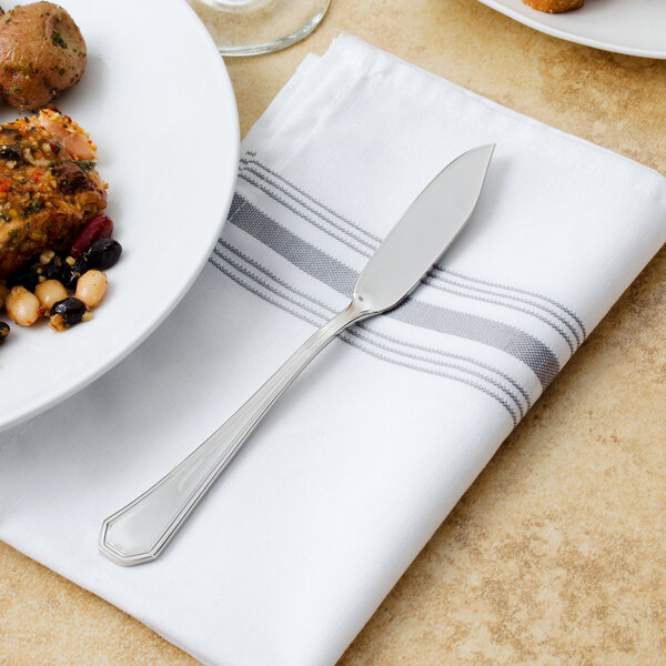 A Walco stainless steel fish knife on a napkin next to a plate of food.