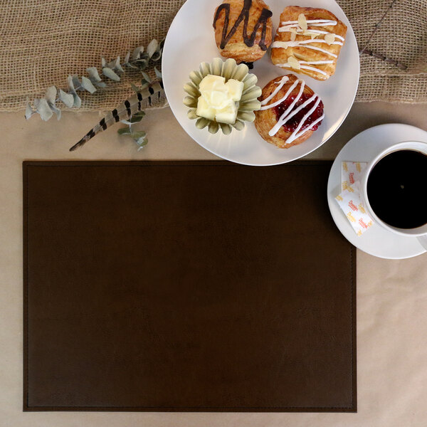 A cup of coffee and pastries on a brown faux leather placemat.