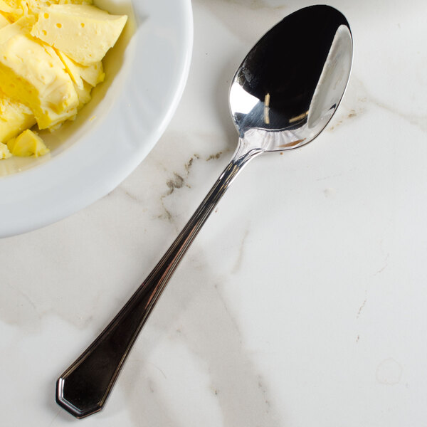 A Walco Prim stainless steel serving spoon next to a bowl of butter on a counter.