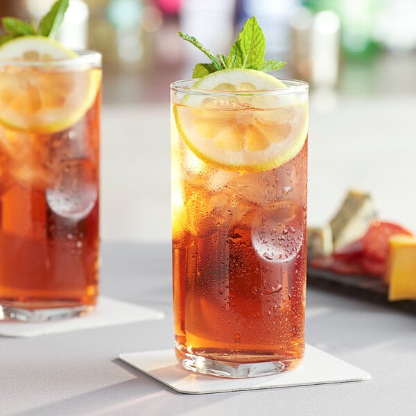 Two Acopa beverage glasses of iced tea with lemon slices and mint leaves.