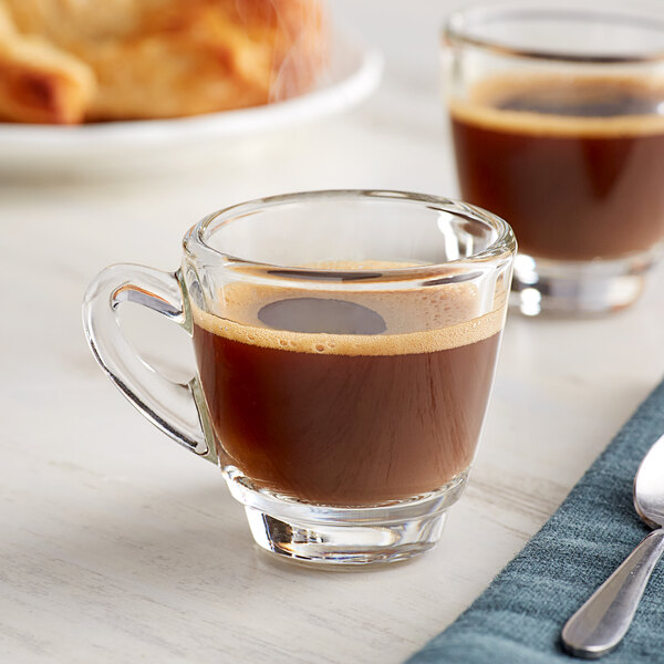 An Acopa espresso cup filled with coffee on a table with a spoon and fork.