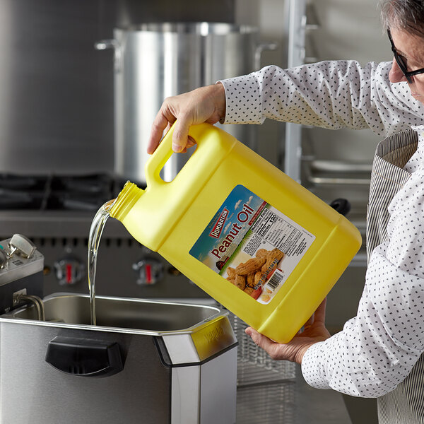 A person pouring Admiration peanut oil into a fryer.