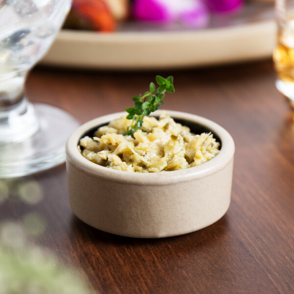 A stackable black Chef & Sommelier stoneware ramekin filled with food on a table.