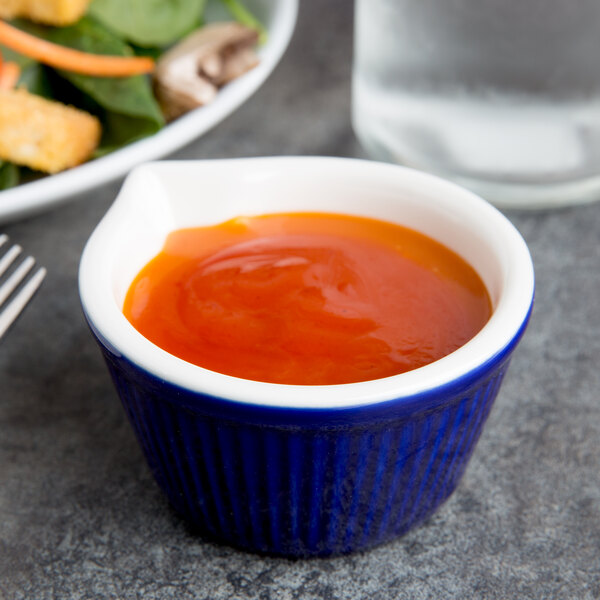 A Tuxton cobalt fluted ramekin filled with red sauce on a table with a plate of salad.