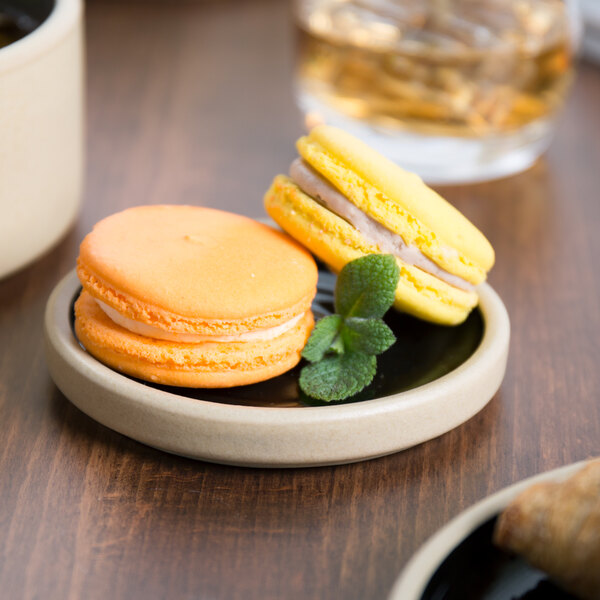 A Chef & Sommelier black stoneware plate with a yellow and white macaroon and a croissant on it.