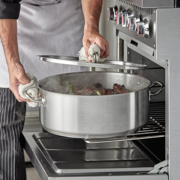 A person using a Vigor stainless steel brazier to cook food.