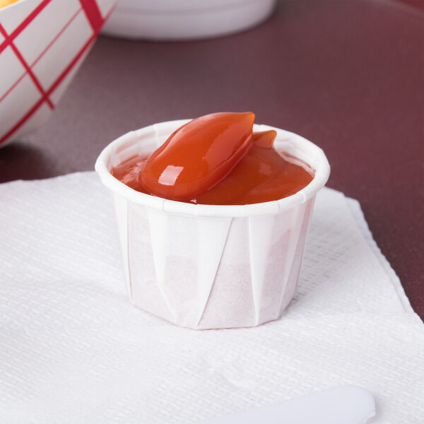 A Solo white paper portion cup filled with ketchup on a white surface.