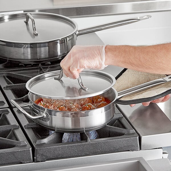 A person using a Vigor stainless steel saute pan with lid and helper handle to cook.