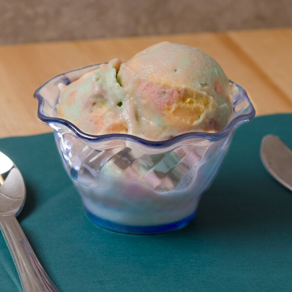 A transparent blue tulip dessert dish filled with ice cream with a spoon in it.