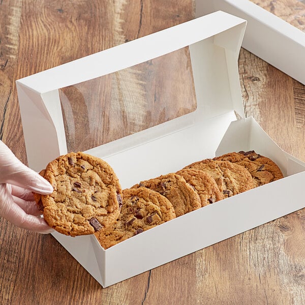 A hand placing a cookie in a white bakery box.