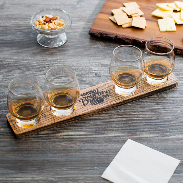 A wooden board with Reserve by Libbey Kentucky Bourbon Trail glasses and snacks on a table.