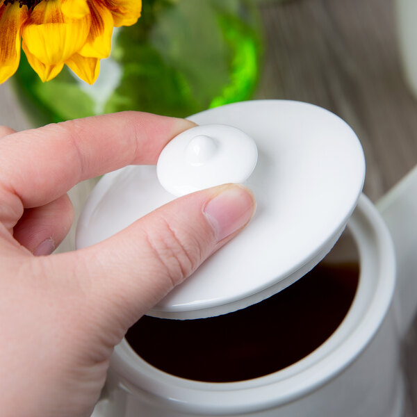 A hand holding a Villeroy & Boch white porcelain teapot lid.