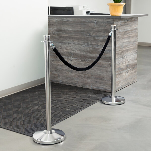 A silver and black rope-style crowd control stanchion with a Lancaster Table & Seating pole.