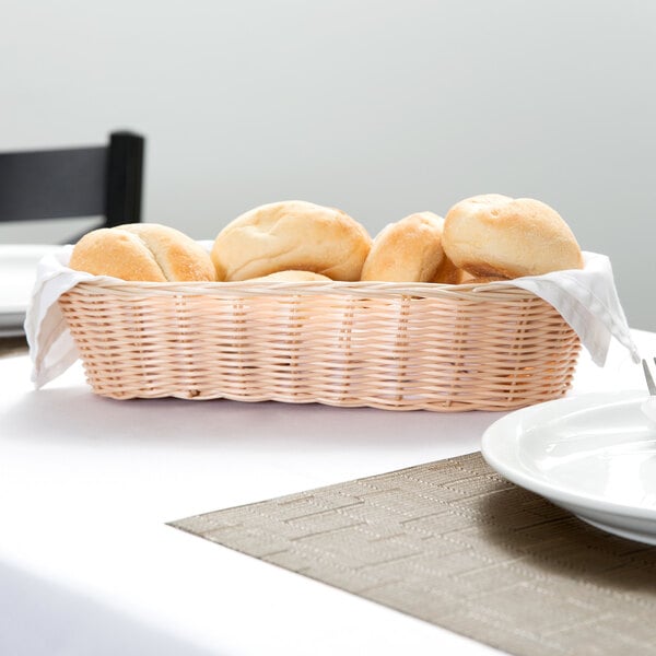 A white table with a white plate and a Tablecraft woven rattan-like bread basket on it.