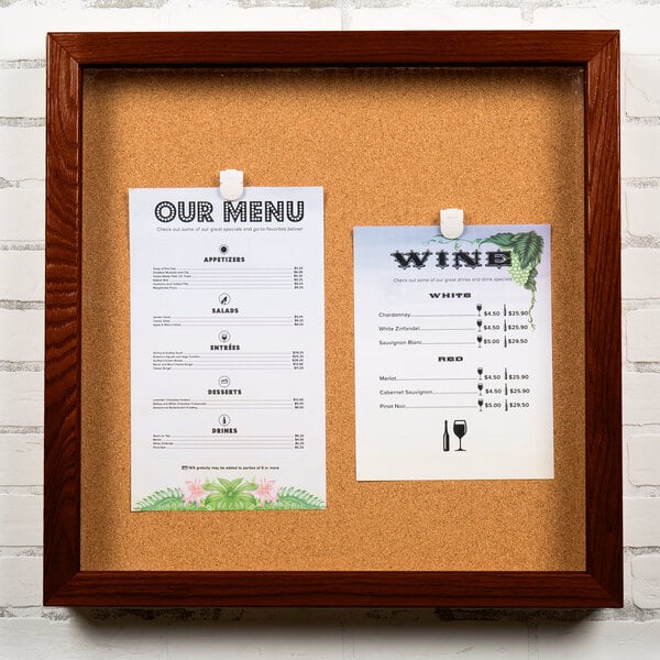 An Aarco cherry wood enclosed bulletin board with a cork background and a framed menu.