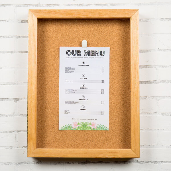 An Aarco natural oak enclosed cork board with a menu on it.