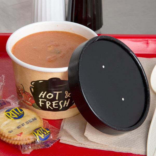 A tray with a bowl of soup and crackers with a black and white dotted lid on top.