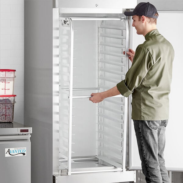 A man in a professional kitchen opening a refrigerator with a Regency unassembled sheet pan rack inside.