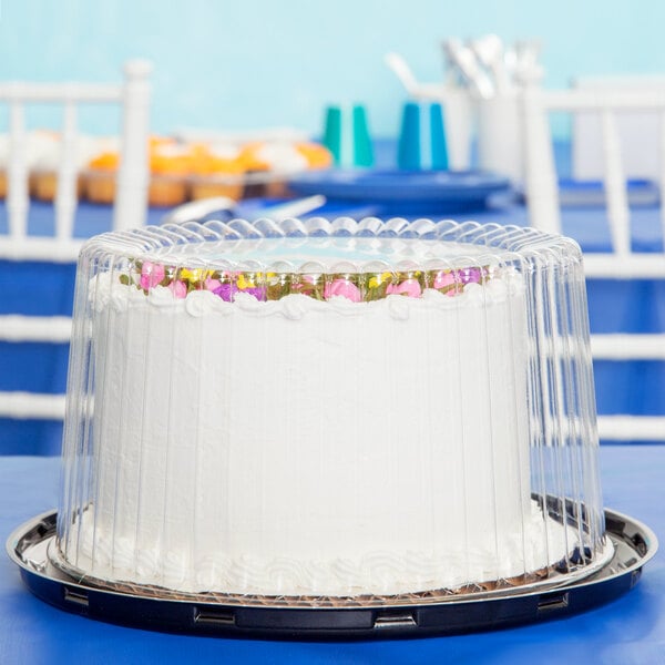 A white cake with flowers on a tray with a clear plastic cover.