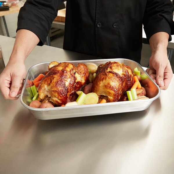 A person holding a Vollrath aluminum roasting pan of cooked chicken and vegetables.