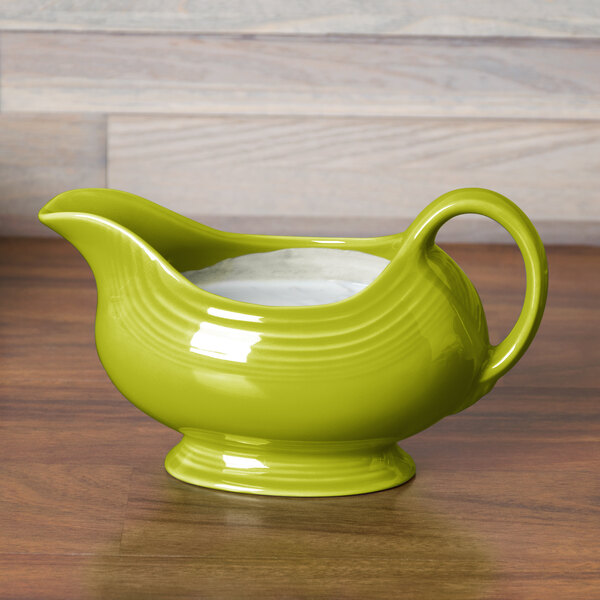 A lemongrass green Fiesta gravy boat with a handle and lid on a wood surface.