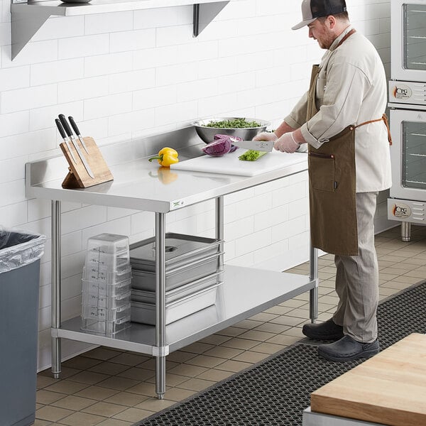 A man in a chef's uniform using a Regency stainless steel work table in a kitchen.