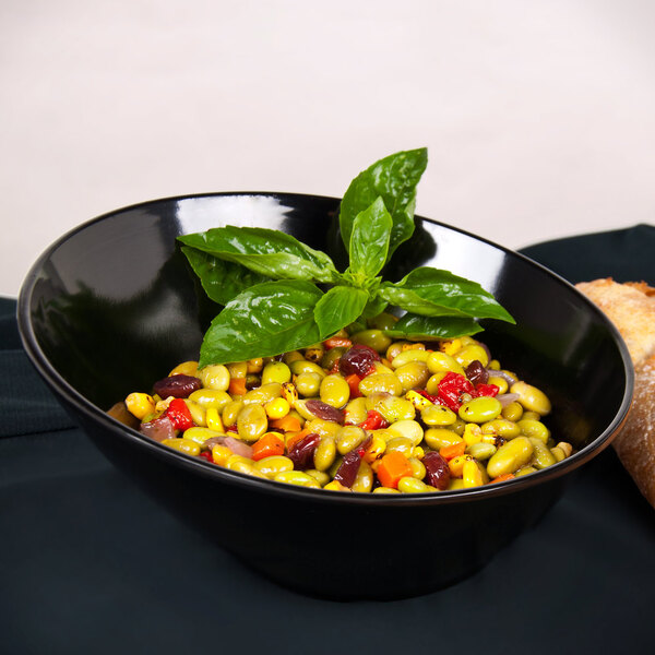 A close up of a black slanted melamine bowl filled with beans and vegetables.
