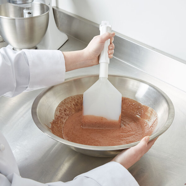 A person using a Carlisle white paddle to mix brown liquid in a bowl.