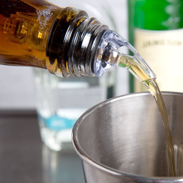 A person using a Tablecraft Proper Pour liquor pourer to pour liquid into a metal cup on a table.