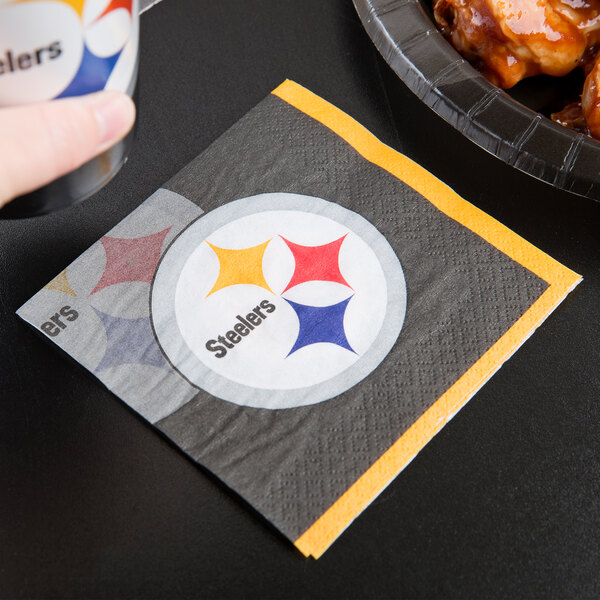A Pittsburgh Steelers beverage napkin on a counter next to a plate of chicken wings.