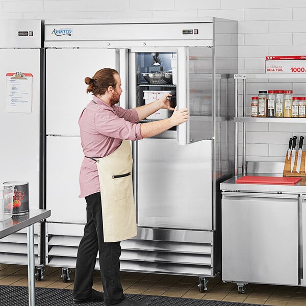 A man in a professional kitchen opening an Avantco stainless steel half door reach-in freezer.