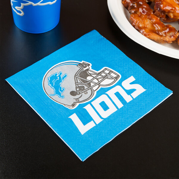 A blue Creative Converting Detroit Lions luncheon napkin with a football helmet logo next to a plate of chicken wings.